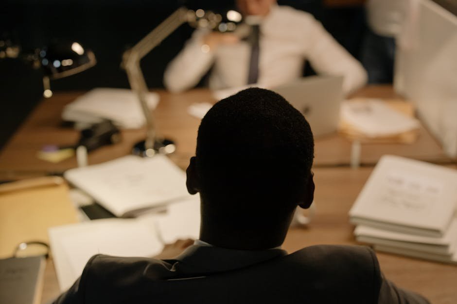 Consultant en sécurité électronique passant en revue des documents techniques lors d'une réunion d'audit dans un bureau à la lumière tamisée